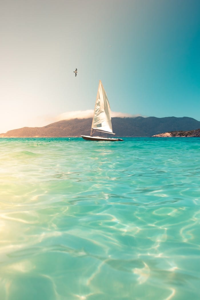 service-06 A sailboat glides across turquoise seas beneath a clear sky, ideal for tranquil travel and vacation scenes.